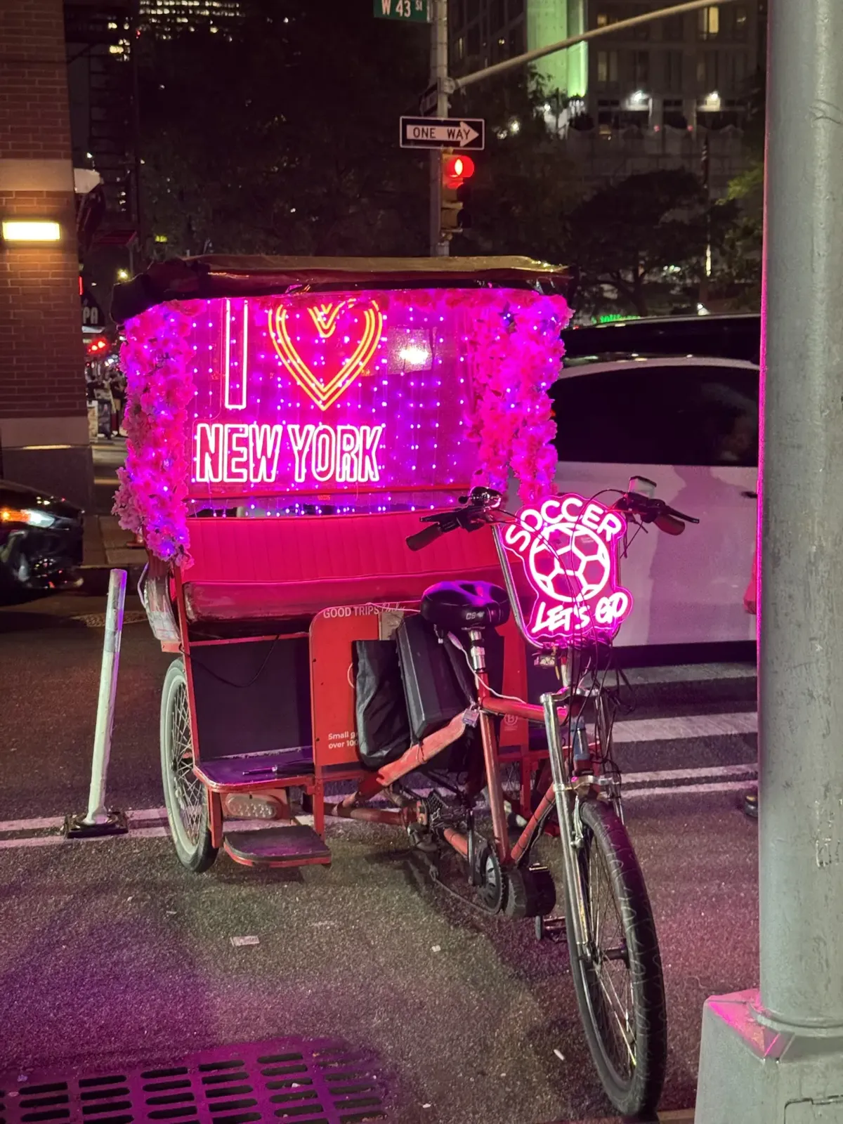1 Hour Pedicab Tour: Central Park or Midtown: Pedicab decorated with pink flowers and an I Love New York neon sign, parked on West 43rd Street at night